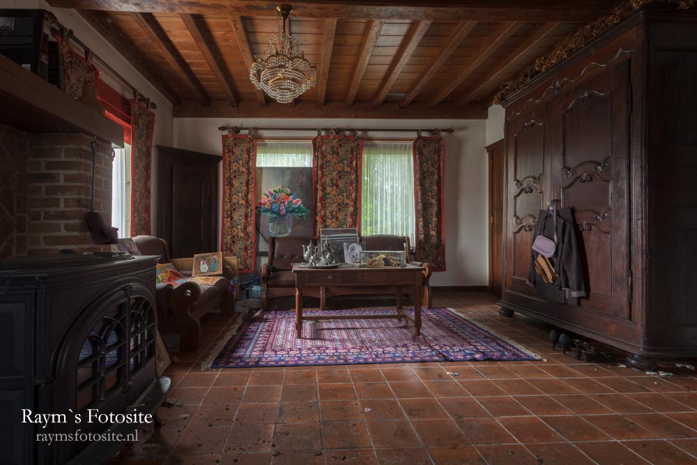 Manoir Marinelle, urbexlocatie in België. De huiskamer met wat schilderijen, en ook op diverse plekken nog wat kleding.