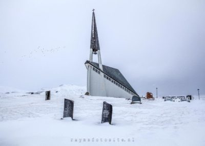 Een prachtige kerk in Ijsland met grafstenen ervoor in de sneeuw.