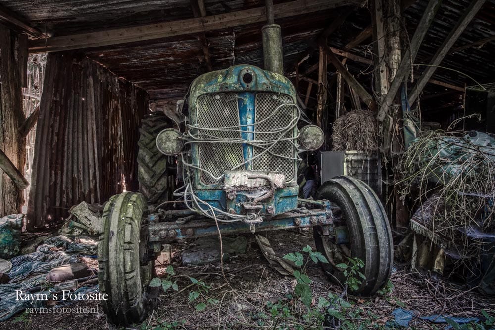 Een oude tractor bij een verlaten schuur op het terrein.